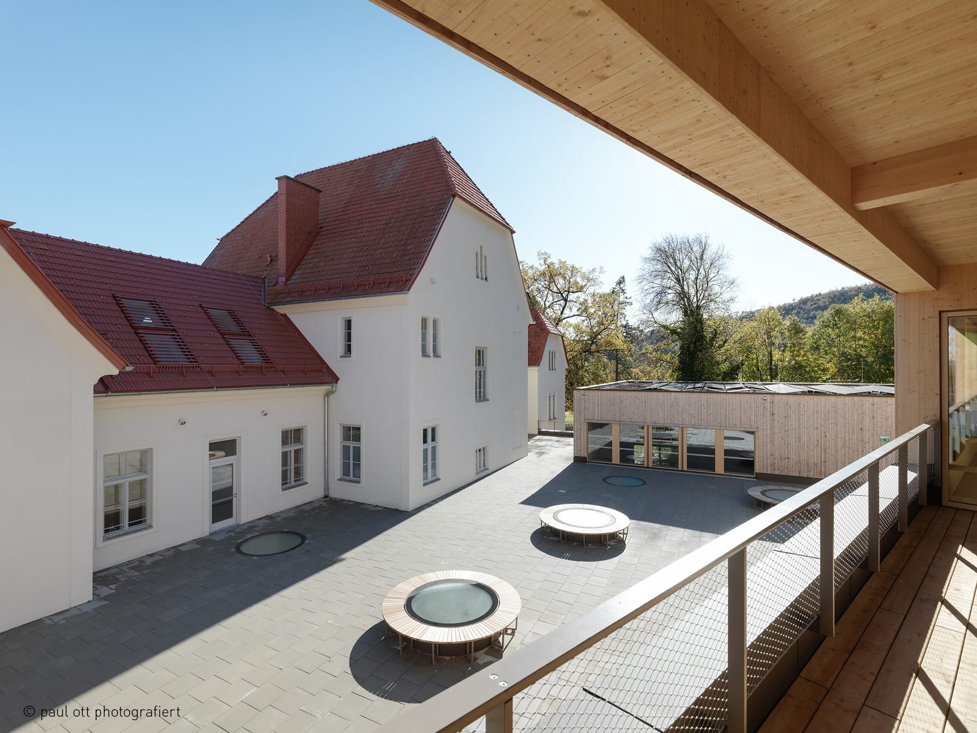 Aufnahme des Innenhofs des LFS in Graz vom Balkon aus. Zu sehen sind fünf runde, begehbare Oberlichter. Drei davon wurden mit erhöhter Unterkonstruktion gefertigt, um mit ihnen eine Sitzgelegenheit zu schaffen.